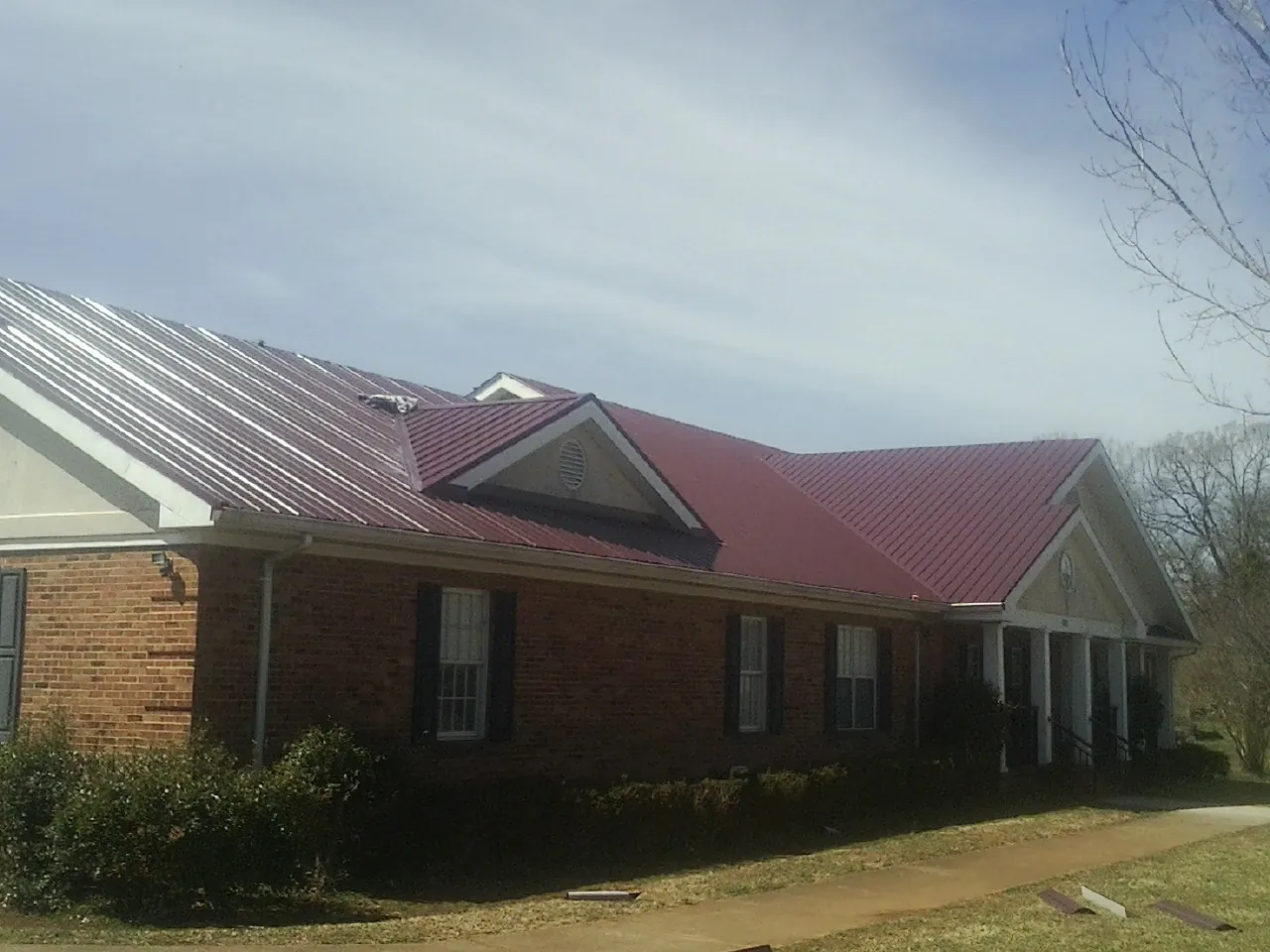 Red metal roof with gabled entries on a long brick building, from a Hail Damage Roof Repair job in Jacumba