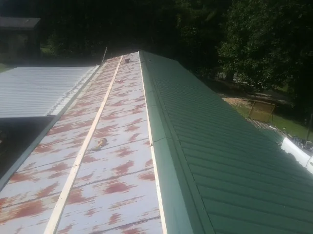 Old rusted panels beside newly installed green metal roofing — Wind Damage Roof Repair by Roofing Brothers in Jacumba