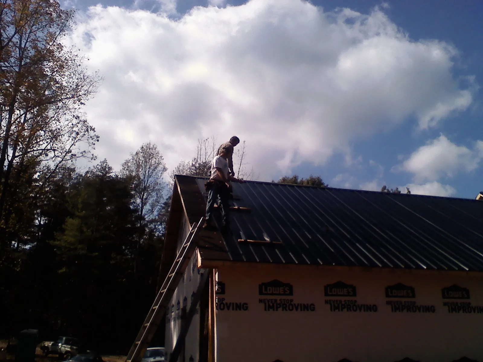 Roofer fastening dark metal panels high against a cloudy sky, from a Roof Inspection job in Jacumba